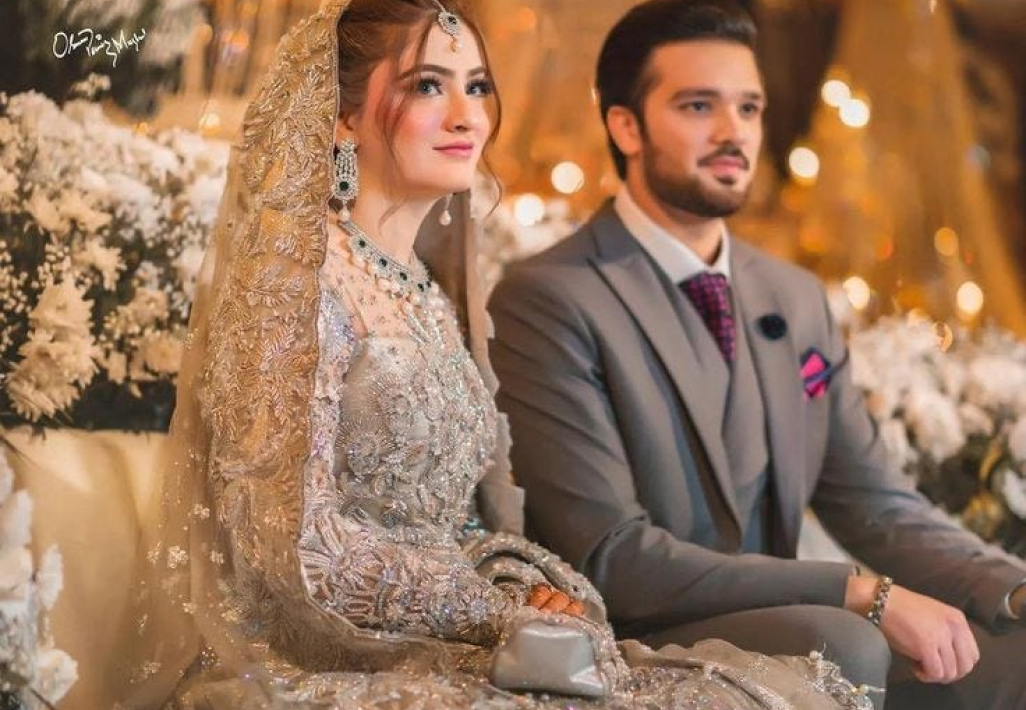 Pakistani bride in an embellished silver gown seated with the groom at a wedding venue